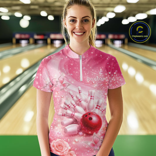 Female model in a bowling lane wearing a pink quarter zip bowling shirt with butterfly and sparkling diamond bowling strike design.
