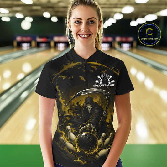 Front view of a female model wearing a black and yellow bowling quarter zip shirt showcasing a grim reaper with a blazing bowling ball striking scattered pins amid swirling flames in a bowling lane.