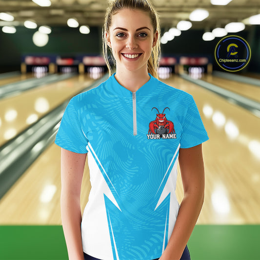 Front view of a happy female model in a bowling alley wearing a blue custom quarter-zip bowling shirt with a funny aggressive crawfish holding a bowling ball in a sportswear-style design.