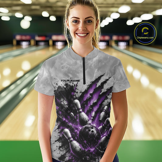 Front view of a female model wearing a gray bowling quarter zip shirt featuring a dramatic purple bowling ball and pins graphic with claw-mark artwork in a bowling lane.