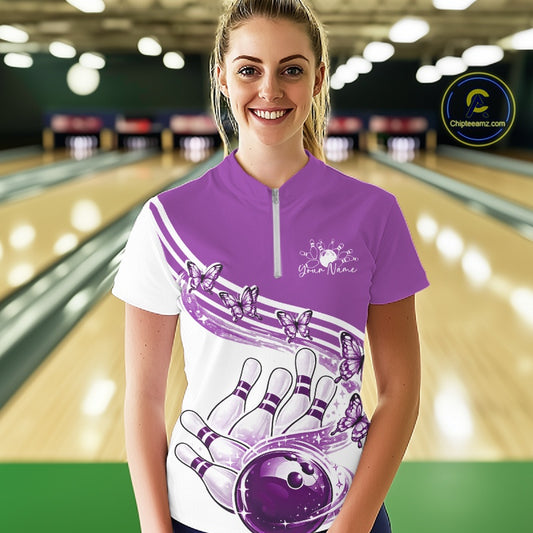 Female model in a white and purple bowling quarter zip featuring butterfly graphics and bowling artwork, front view at the bowling lane