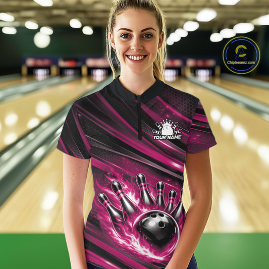 Female model in a bowling lane wearing black and pink quarter zip shirt, front view showcasing fiery bowling ball hitting pins dynamic artwork