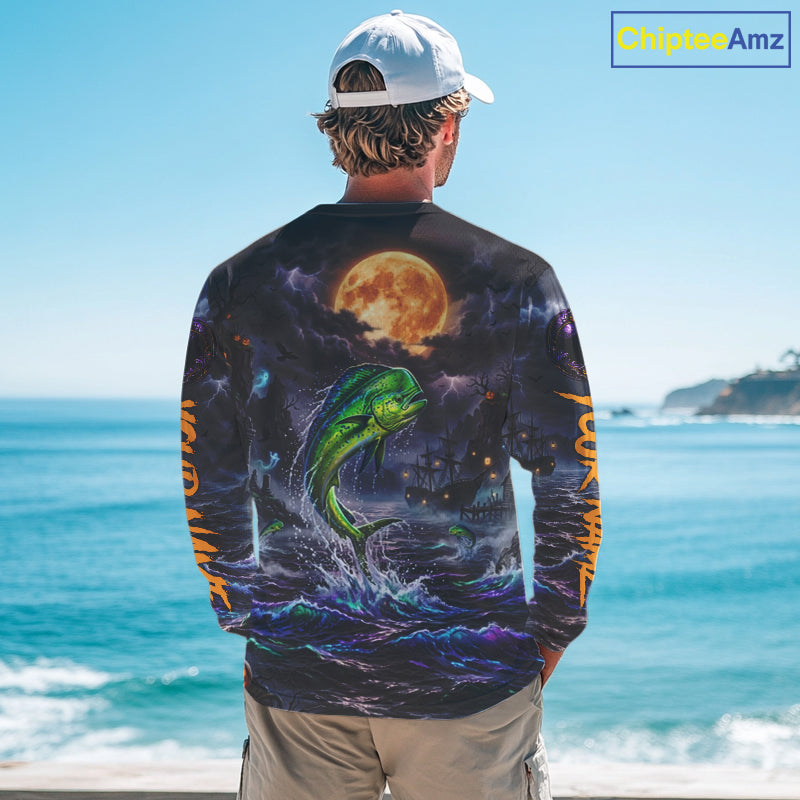 A man stands with his back to the camera wearing a long-sleeve graphic shirt featuring a green fish jumping in front of a full moon over the ocean. The shirt has orange text down the sleeves and is shown against a beach background with a 'ChipteeAmz' watermark in the top right corner.