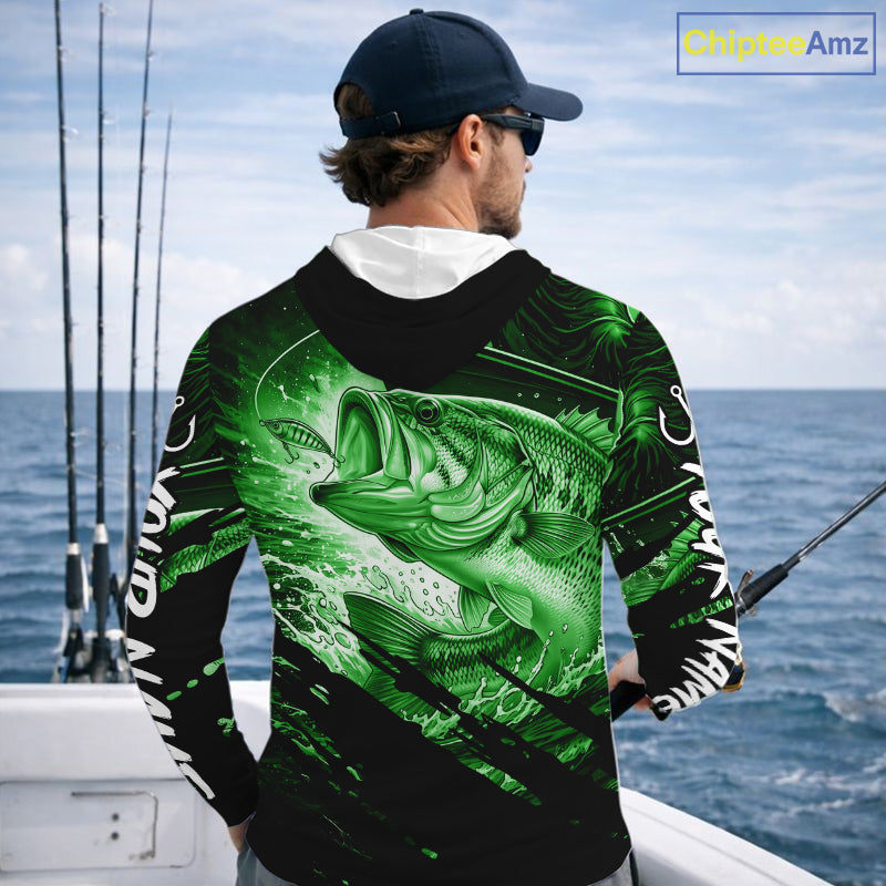 Person wearing a green and black bass hooded fishing shirt with a fish design, standing by the ocean.