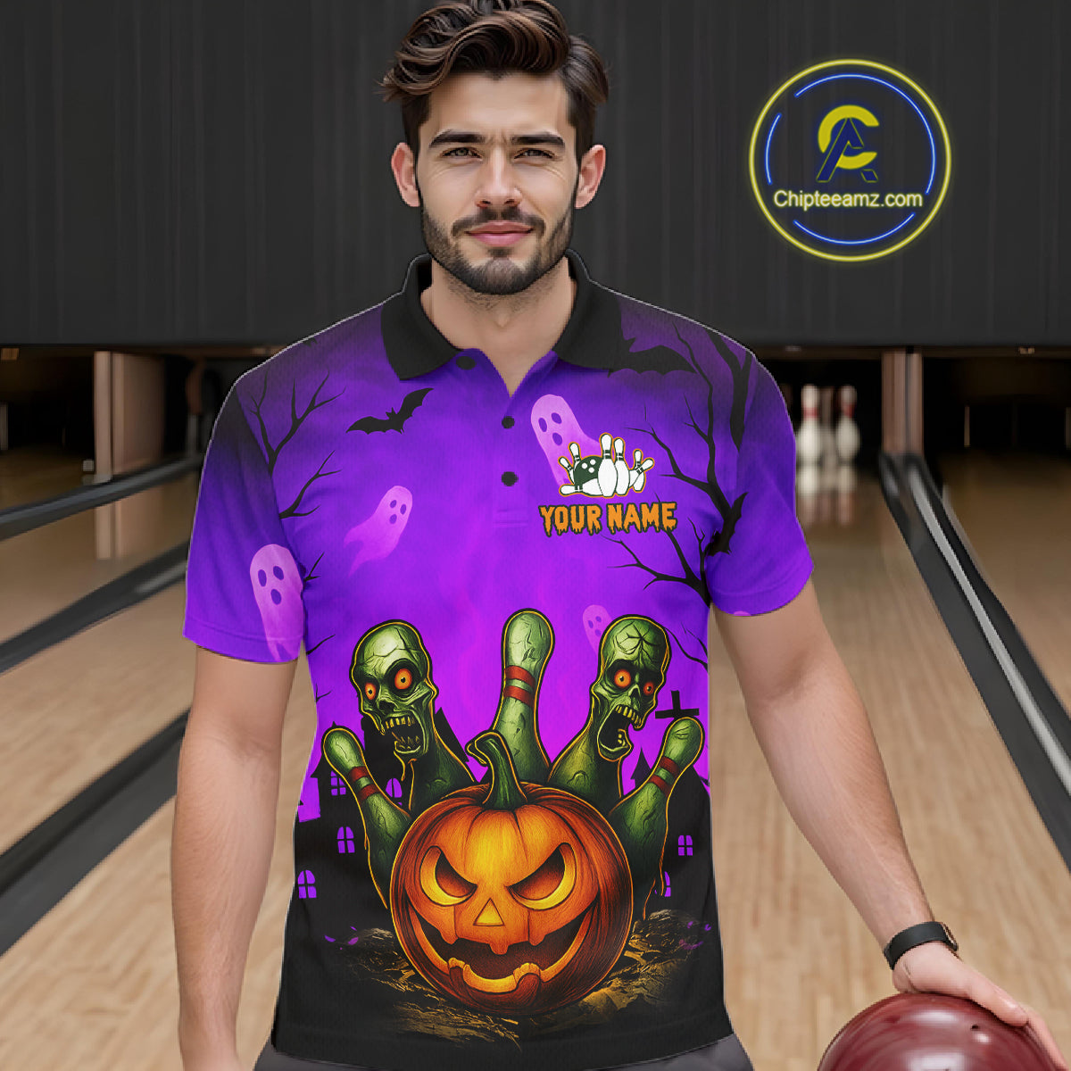 A man wearing a purple Halloween-themed polo shirt with a graphic of a jack-o'-lantern, green zombies, ghosts, and bats, standing in a bowling alley. 
