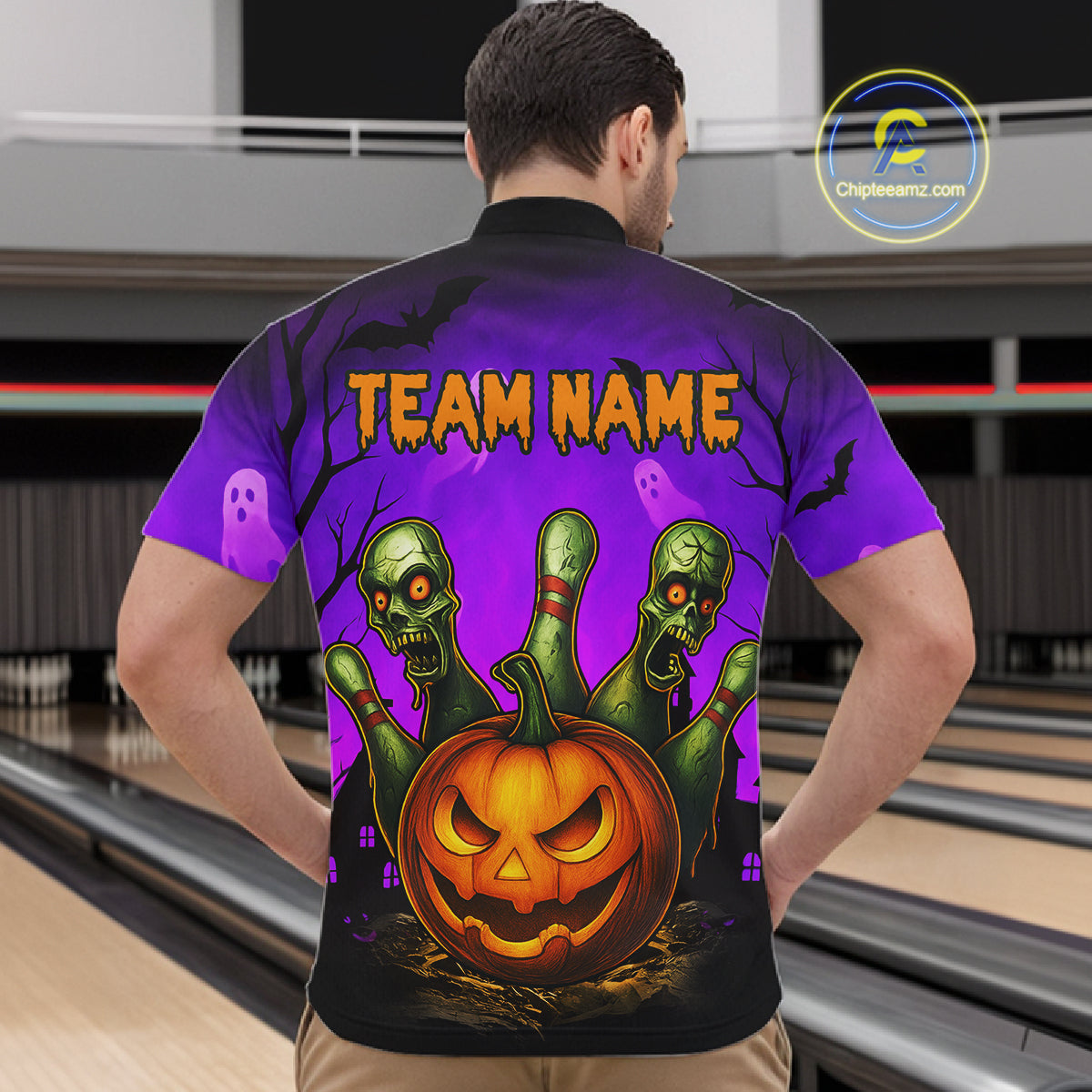 A man viewed from behind wearing a short-sleeve bowling shirt with a Halloween graphic. The shirt features a purple and black gradient background with three green zombie fingers reaching up from a carved orange jack-o'-lantern, plus the text 'TEAM NAME' in orange.