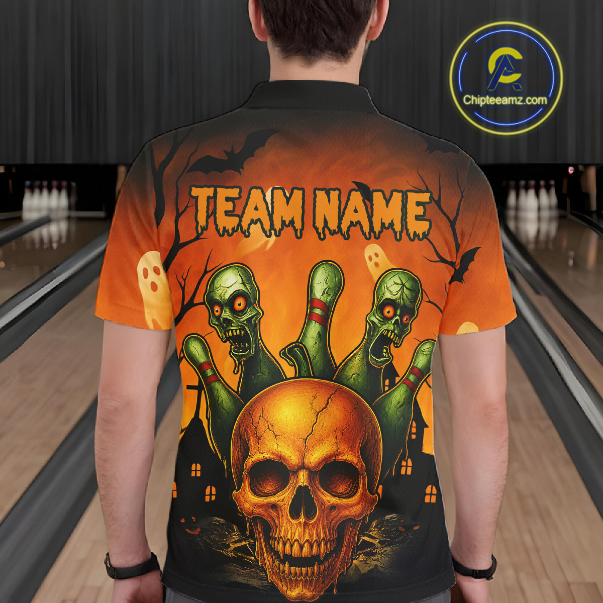 A person viewed from behind wearing a short-sleeve black polo shirt with a large Halloween-themed graphic print. The design features a glowing orange skull, green zombie hands, ghosts, bats, and the text 'TEAM NAME' on an orange-to-black gradient background.