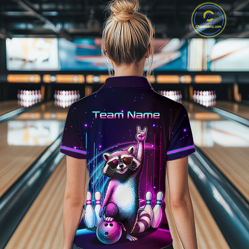 A woman viewed from behind wearing a custom bowling-themed polo shirt in a bowling alley. The back of the dark purple shirt features a colorful graphic of a raccoon bowling with pins and the text 'Team Name'.