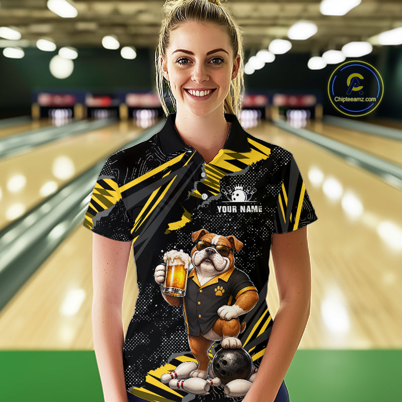 A woman wearing a custom bowling-themed polo shirt with a bulldog graphic holding a beer mug, set against a blurred bowling alley background. The shirt is black with yellow accents and features a customizable name patch.