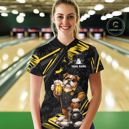 A woman standing in a bowling alley wearing a custom black and yellow short-sleeve bowling shirt with a bulldog graphic holding a beer mug and a bowling ball. The shirt has a custom name placeholder on the chest.