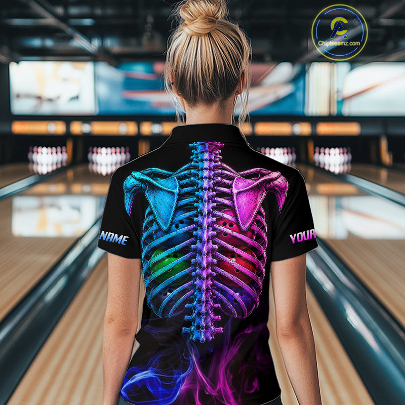A woman viewed from behind wearing a black short-sleeve polo shirt with a large colorful neon skeleton ribcage graphic on the back, standing in a bowling alley.
