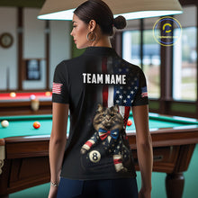 Load image into Gallery viewer, A back view of a custom black billiards polo shirt worn by a female model turned away from the camera in front of a pool table. The shirt features a large distressed US flag pattern on the back, with a large white 'TEAM NAME' text placeholder. The cat and 8-ball motif is at the bottom of the flag design. The background is a billiards room with a table and hanging lights.