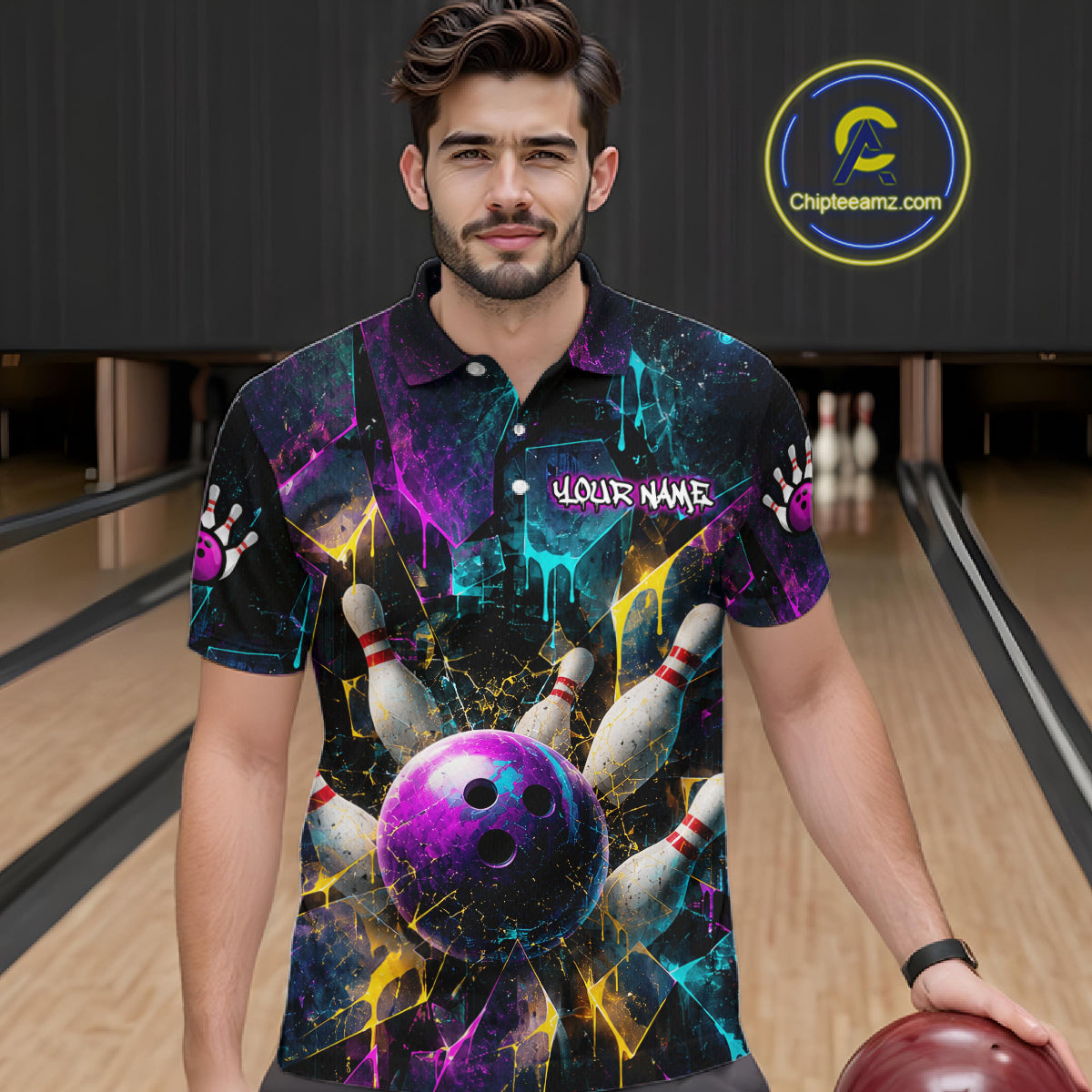 A man wearing a short-sleeve bowling-themed polo shirt with a colorful cosmic print of bowling balls and pins, standing in a bowling alley. The shirt features a purple bowling ball graphic, white bowling pins, and a 'YOUR NAME' placeholder on the chest.
