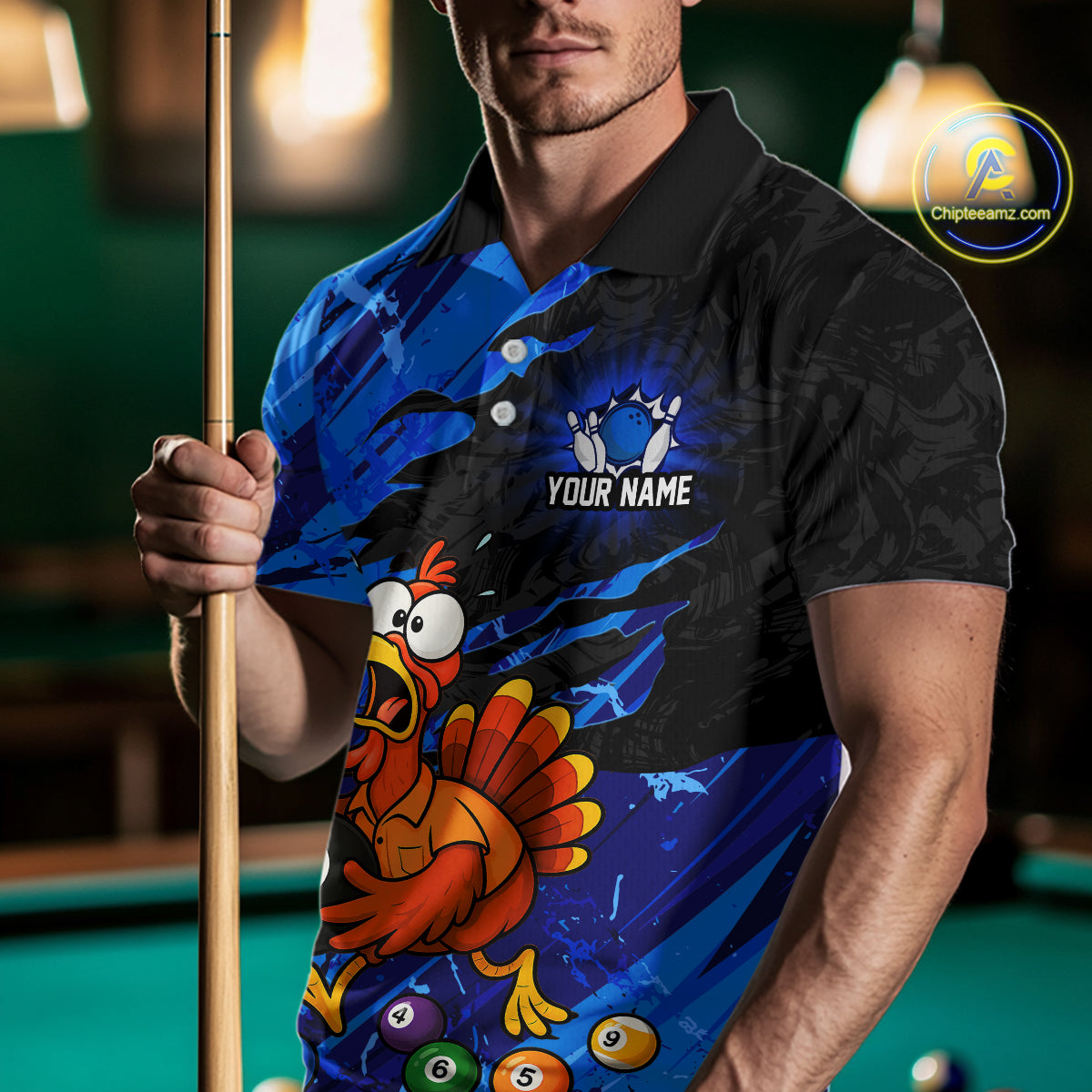 A man wearing a custom blue and black polo shirt with a cartoon turkey graphic and bowling pins, holding a pool cue in a dimly lit billiards room. 
