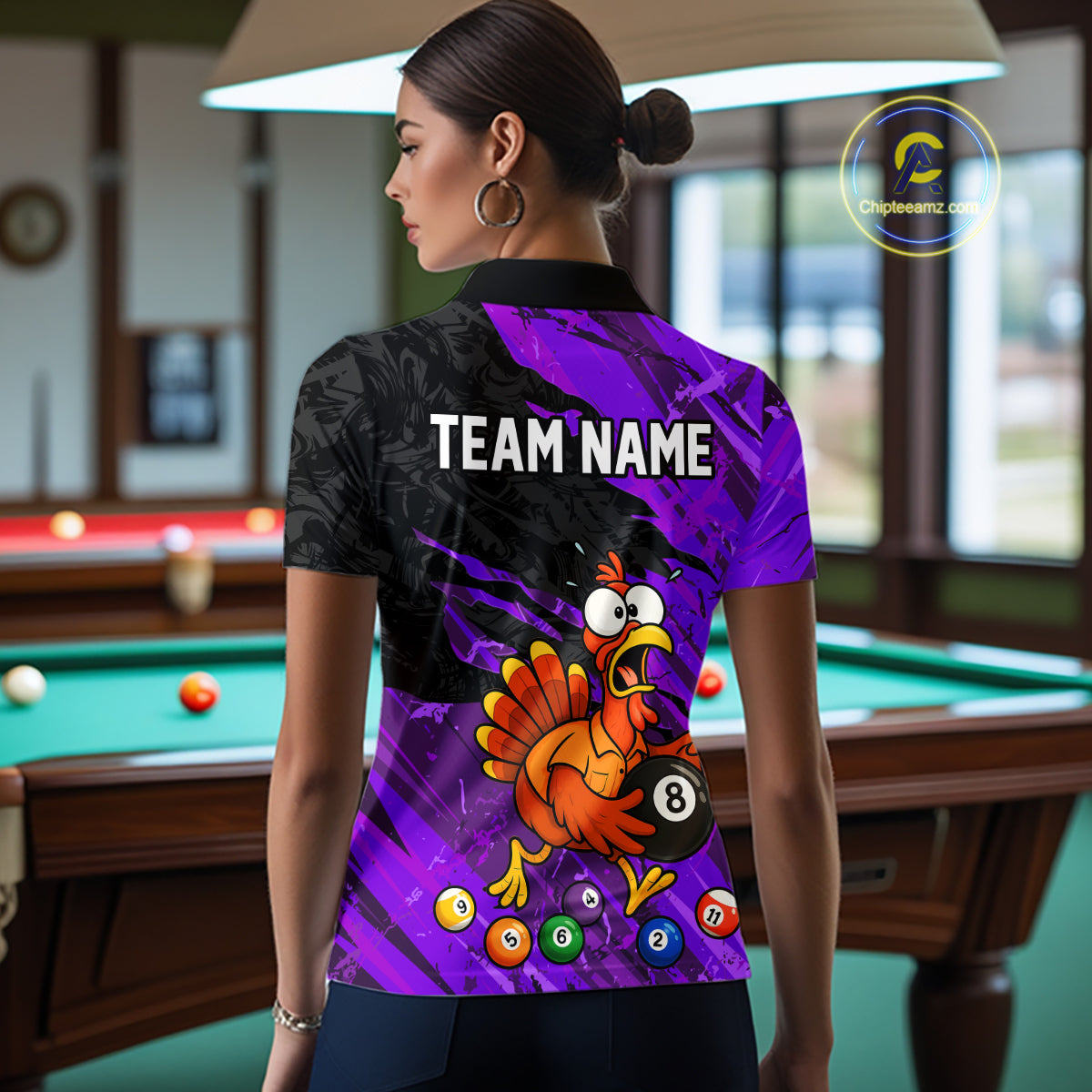 A woman stands in a billiards room wearing a custom-printed short-sleeve polo shirt from the back. The shirt features a vibrant purple and black background with a cartoon turkey graphic, pool balls, and the text 'TEAM NAME'.