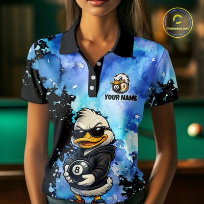 A woman wearing a short-sleeve polo shirt with a blue and black watercolor-style graphic print featuring a cartoon duck wearing sunglasses and holding an 8-ball, with the text 'YOUR NAME' and a logo on the chest. The background is a blurred indoor pool room setting.
