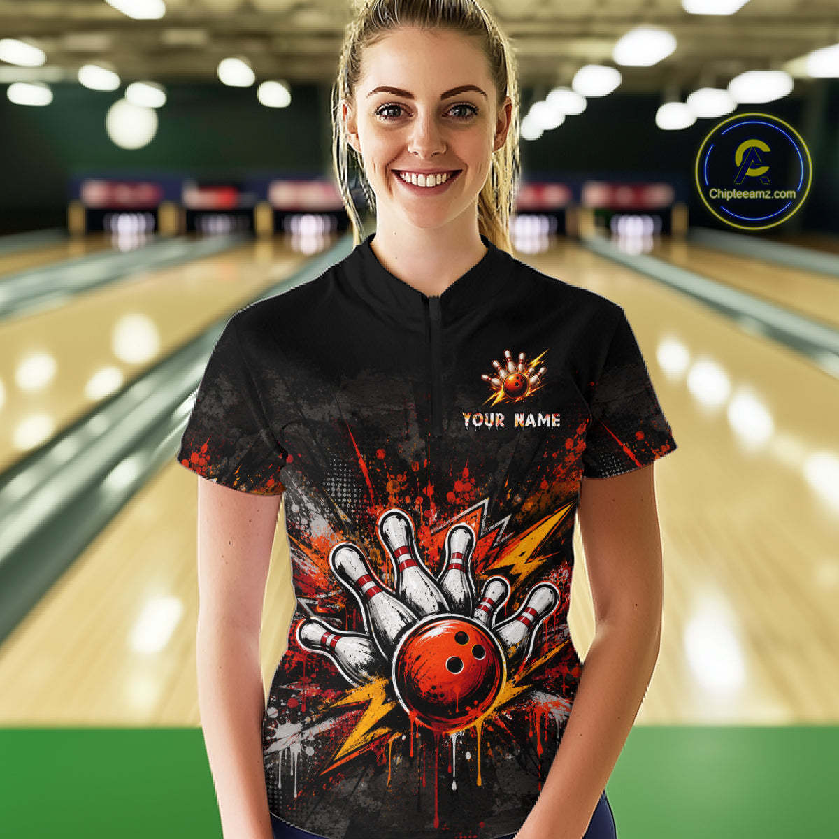 A woman stands in a bowling alley wearing a black short-sleeve bowling shirt with a red, white, and orange bowling pin and ball graphic on the front, along with 'YOUR NAME' text and a logo. 