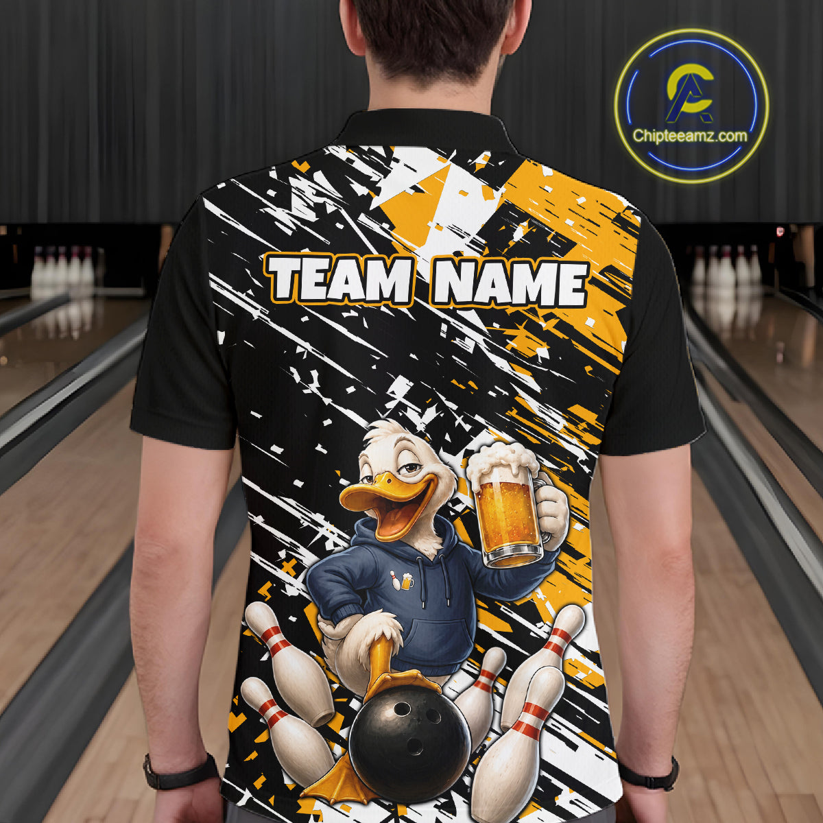 A person standing in a bowling alley wearing a black short-sleeve polo shirt with a large back graphic. The graphic features a cartoon duck holding a beer mug and bowling ball, surrounded by bowling pins, with the text 'TEAM NAME' across the upper back.