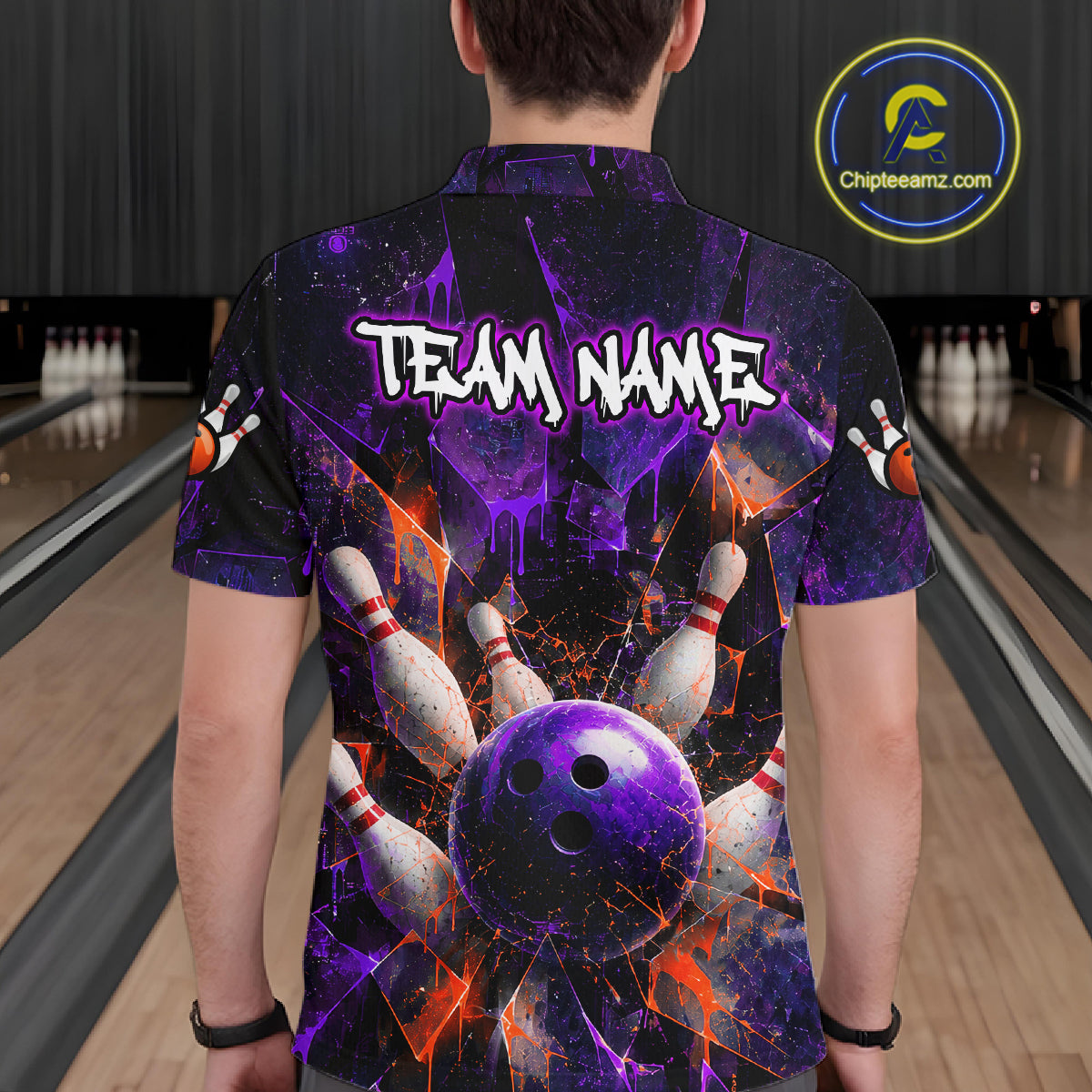 A person standing in a bowling alley viewed from behind, wearing a short-sleeve button-up shirt with a bowling-themed graphic print. The shirt features a purple bowling ball, white pins, orange splatters, and the text 'TEAM NAME' across the upper back.