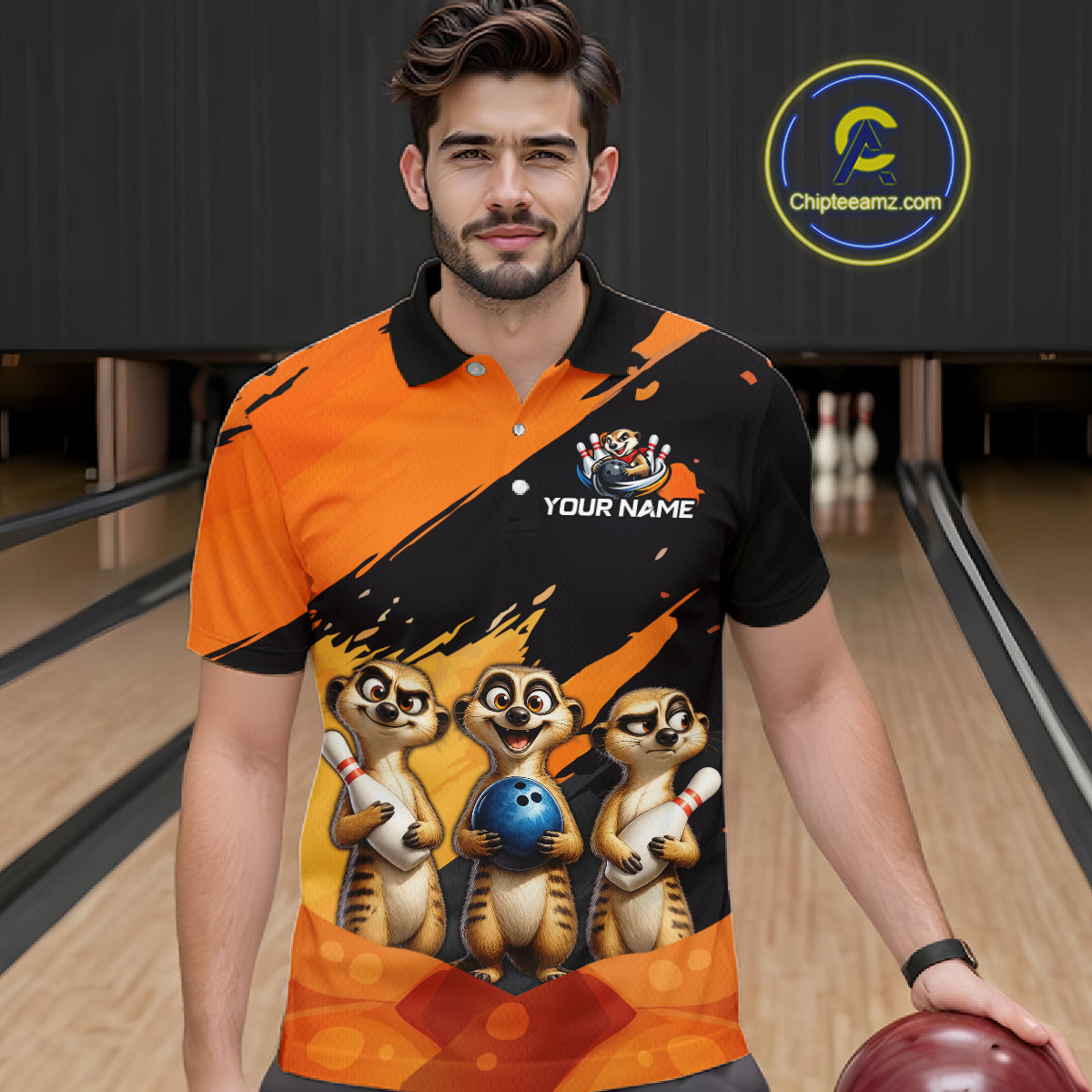 A man in a bowling alley wearing a custom orange and black short-sleeve bowling shirt with a graphic of three cartoon meerkats holding bowling balls. The shirt has a black collar and a customizable name printed on the chest.