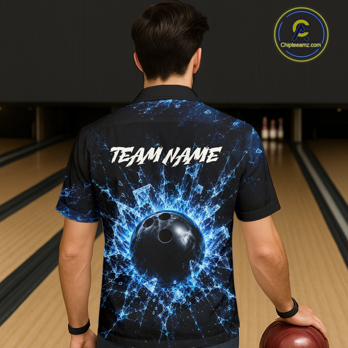 Person wearing a bowling shirt with a blue and black design and 'TEAM NAME' text, holding a bowling ball in a bowling alley.