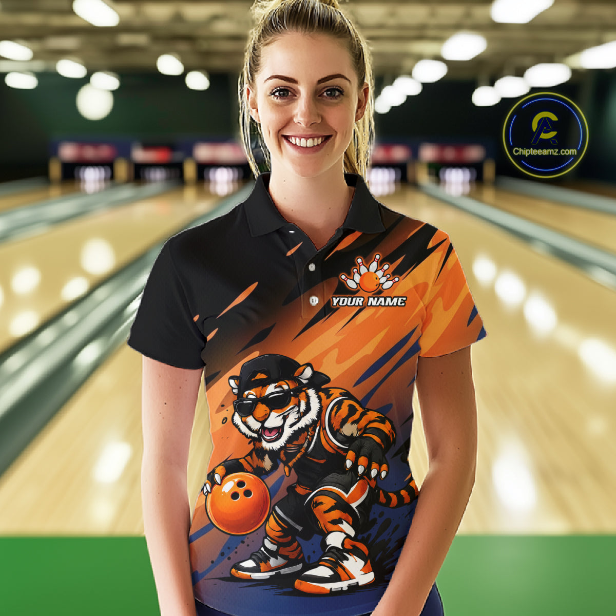 A woman stands in a bowling alley wearing a custom short-sleeve polo shirt with a black collar and upper section, transitioning into orange and dark blue graphic panels featuring a tiger mascot holding a bowling ball. The shirt has a placeholder chest print reading 'YOUR NAME'.