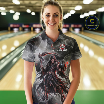 A woman stands in a bowling alley wearing a dark gray and black short-sleeve polo shirt with a grim reaper graphic and the text 'YOUR NAME'. The bowling lanes are blurred in the background