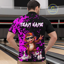 Load image into Gallery viewer, A man viewed from behind wearing a black short-sleeve bowling shirt with a bright purple splatter design, white 'TEAM NAME' text, and a cartoon monkey graphic on the back. Bowling lanes are visible in the background.