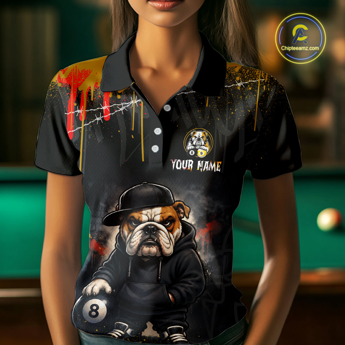 A woman wearing a black short-sleeve polo shirt with a custom graphic print of a bulldog wearing a black hoodie and cap, holding a billiard ball. The shirt features a custom name placeholder and a circular bulldog logo on the chest, set against a blurred pool table background.
