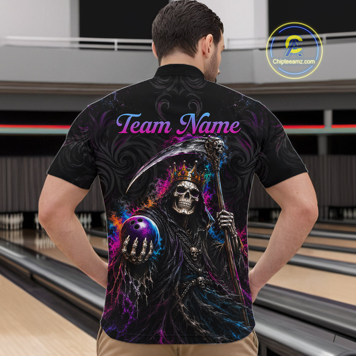 A man viewed from behind wearing a black short-sleeve polo shirt with a large colorful Grim Reaper graphic and the text 'Team Name' across the back, standing in a bowling alley. 
