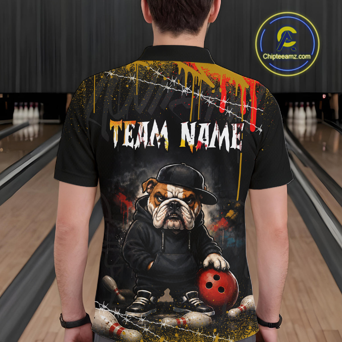 A person viewed from behind wearing a black short-sleeve polo shirt with a large bowling-themed graphic on the back. The design features the text 'TEAM NAME' in white with red and yellow accents, a bulldog in a black hoodie holding a red bowling ball, barbed wire, paint drips, and bowling pins at the bottom.