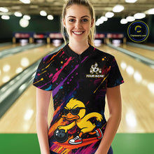 Load image into Gallery viewer, A woman stands in a bowling alley wearing a black short-sleeve bowling shirt with a colorful paint-splatter design and a large yellow duck graphic on the front. The shirt has a white cartoon duck logo and the text 'YOUR NAME' on the chest.