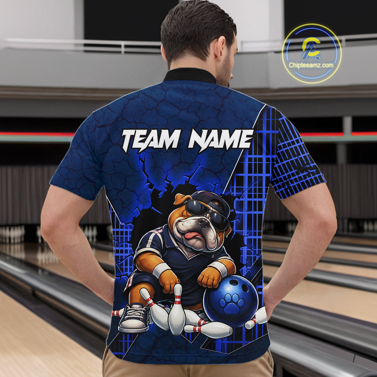 A man viewed from behind wearing a custom blue bowling-themed short-sleeve shirt with a bulldog graphic and 'TEAM NAME' text, set against a bowling alley background.