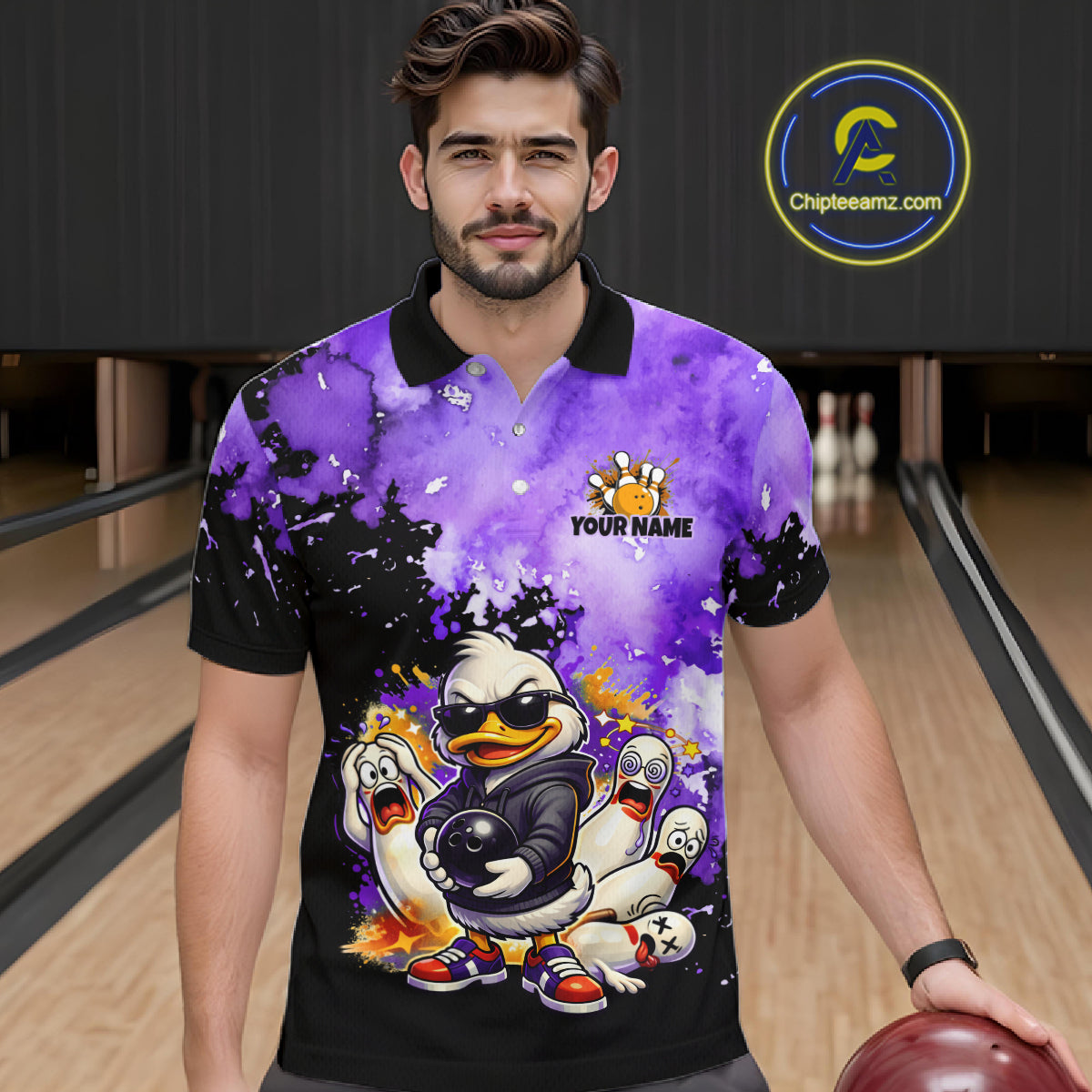 A man wearing a custom bowling-themed short-sleeve polo shirt with a purple and black watercolor splatter design, cartoon ducks, and a 'YOUR NAME' logo, set against a bowling alley background. 