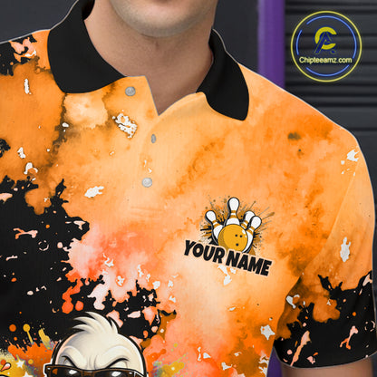 A close-up of a person wearing a short-sleeve polo shirt with an orange and black watercolor splatter design. The shirt has a black collar, silver buttons, a custom bowling-themed graphic with the text 'YOUR NAME' on the left chest
