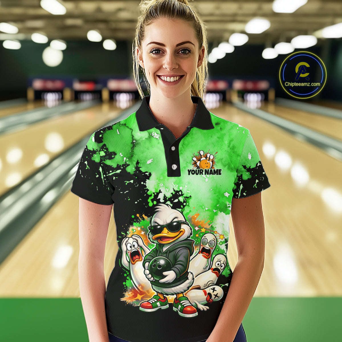A woman stands in a bowling alley wearing a custom short-sleeve polo shirt with a green and black splatter design and a cartoon duck graphic. The shirt has a black collar and sleeve cuffs, with 'YOUR NAME' printed on the chest.