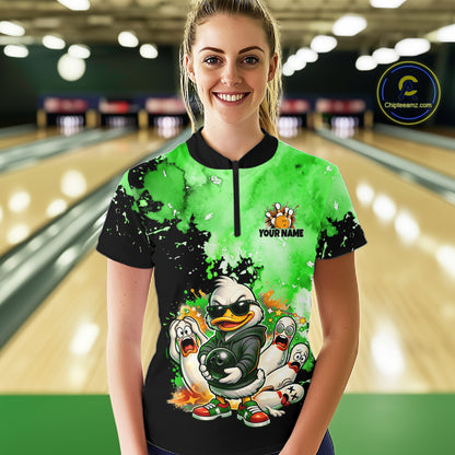 A woman stands in a bowling alley wearing a short-sleeve collared bowling shirt with a black and bright green watercolor splatter design, a cartoon duck mascot, and 'YOUR NAME' text on the chest. 