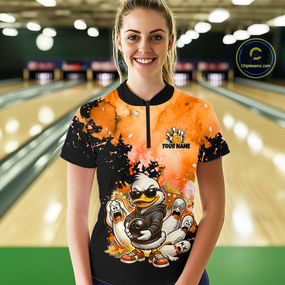 A woman stands in a bowling alley wearing a short-sleeve quarter-zip bowling shirt with a colorful cartoon duck graphic and the text 'YOUR NAME' 