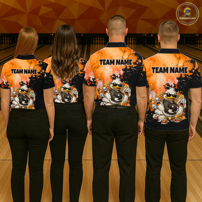 Four people standing with their backs to the camera in a bowling alley, wearing matching bowling shirts with a black and orange flame design, cartoon bowling balls, and 'TEAM NAME' printed on the back.