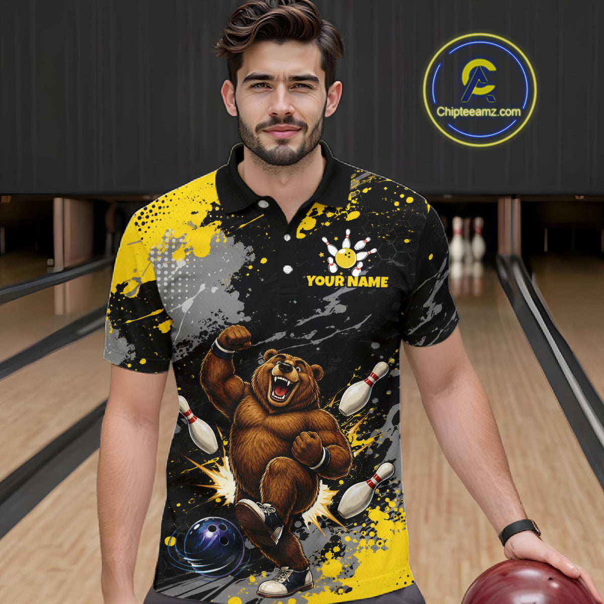 A man wearing a custom bowling-themed short-sleeve polo shirt with a graphic of a bear bowling, yellow and black splatter patterns, and a white paw print logo with 'YOUR NAME' text. The background shows a bowling alley with lanes and pins.