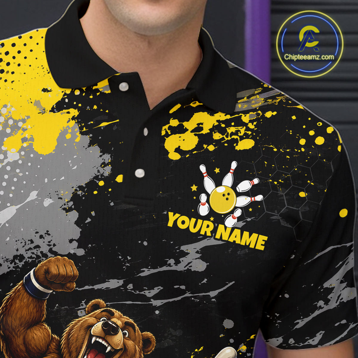 A close-up of a person wearing a black short-sleeve polo shirt with a bold yellow, gray, and white sports graphic print. The shirt features a bowling pin and bowling ball motif with the text 'YOUR NAME' and a cartoon bear graphic on the lower left.