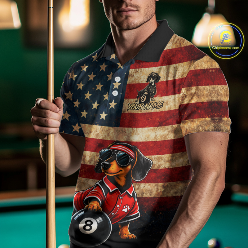 A man in a poolroom wearing a custom polo shirt with a distressed American flag design, featuring a cartoon dachshund wearing a red polo and holding a 8-ball. He is holding a pool cue.