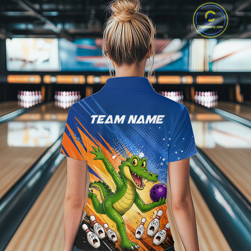 A woman viewed from behind wearing a custom blue bowling-themed short-sleeve polo shirt with a cartoon alligator graphic and the text 'TEAM NAME' on the back, standing in a bowling alley.