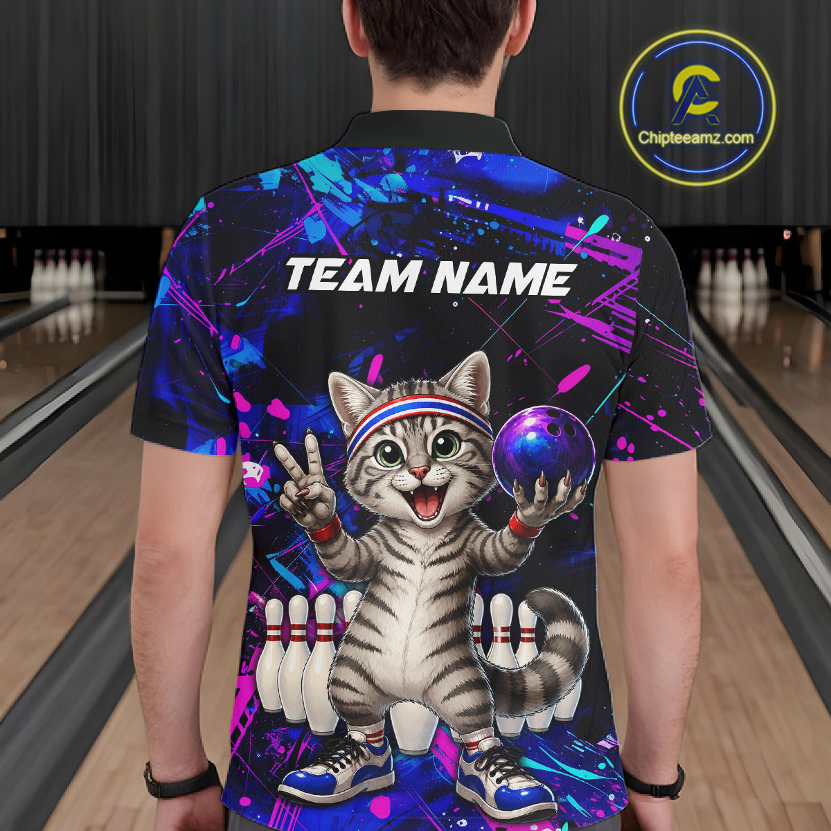Person wearing a colorful bowling-themed shirt with a cat design in a bowling alley.