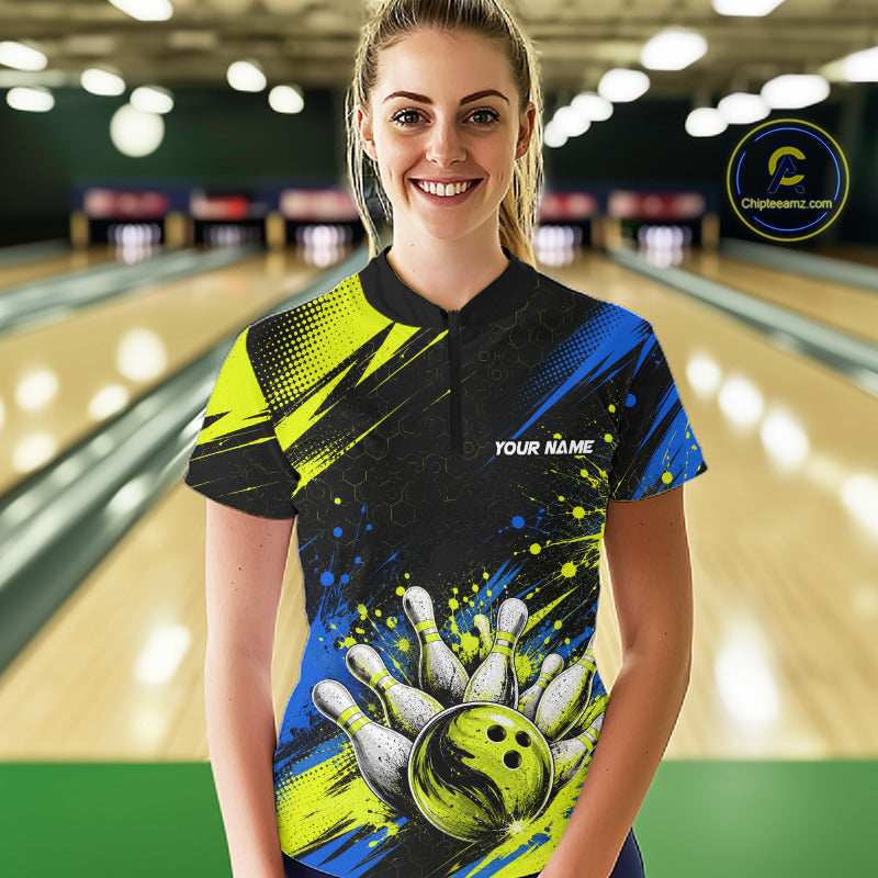 A woman standing in a bowling alley wearing a custom bowling jersey with a black, blue, and neon yellow design featuring a bowling ball and pins graphic. The jersey has 'YOUR NAME' printed on the chest.
