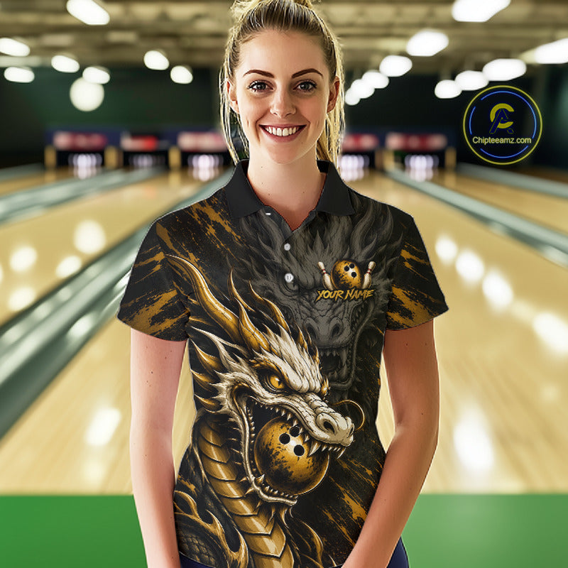 A woman stands in a bowling alley wearing a black short-sleeve polo shirt with a large gold and gray dragon graphic and a small skull motif on the chest. Bowling lanes are blurred in the background, and a circular 'Chipleanic' watermark appears in the top right.