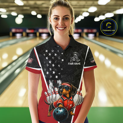 A woman stands in a bowling alley wearing a custom printed bowling-themed polo shirt. The shirt features a black and red design with white stars, a cartoon dachshund bowling dog, and the text 'YOUR NAME'.