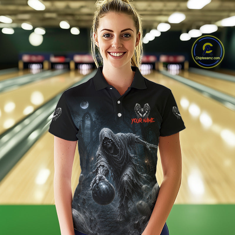 A woman stands in a bowling alley wearing a black short-sleeve polo shirt with a large dark fantasy graphic of a hooded figure holding a bowling ball, plus red placeholder text reading 'YOUR NAME' and small winged logos on the sleeves. 