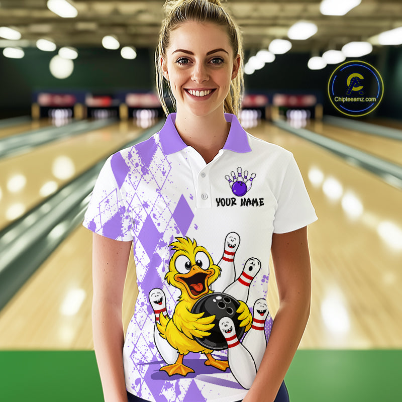 A woman stands in a bowling alley wearing a white short-sleeve polo shirt with purple argyle patterns, a purple bowling pin graphic, and a cartoon yellow duck holding bowling pins and a bowling ball. The shirt also has a 'YOUR NAME' customization placeholder.