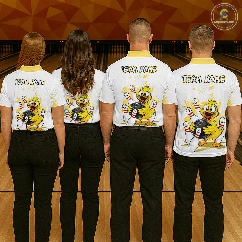 Four people standing with their backs to the camera in a bowling alley, wearing matching white bowling shirts with a yellow collar and a large cartoon bowling character graphic on the back, along with black pants. The shirts have 'TEAM NAME' printed on the upper back.